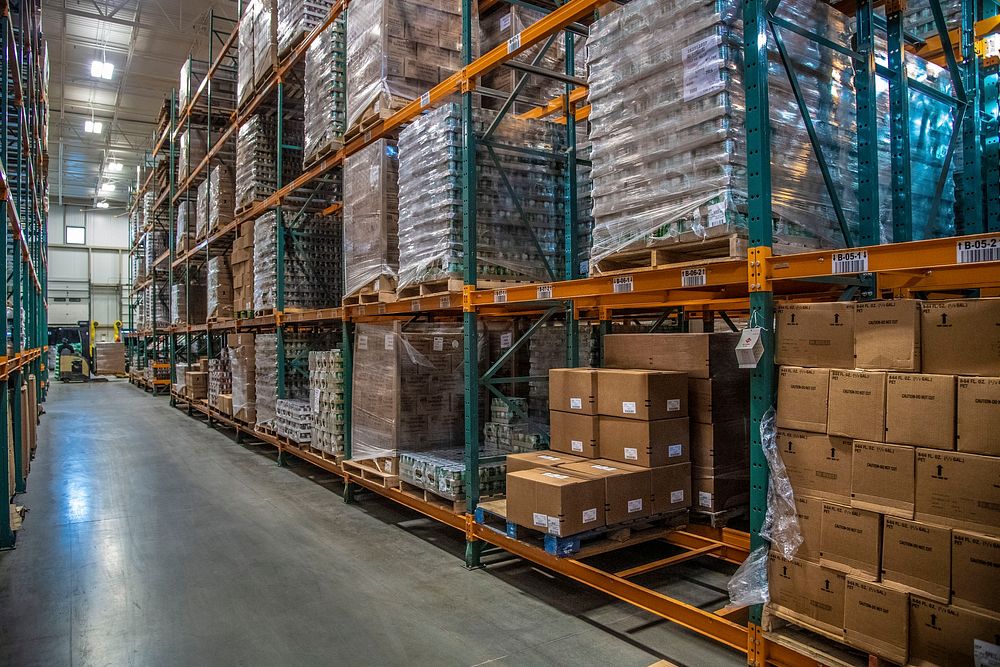 A distribution warehouse aisle lined with pallet racking holding wrapped, labelled stock.