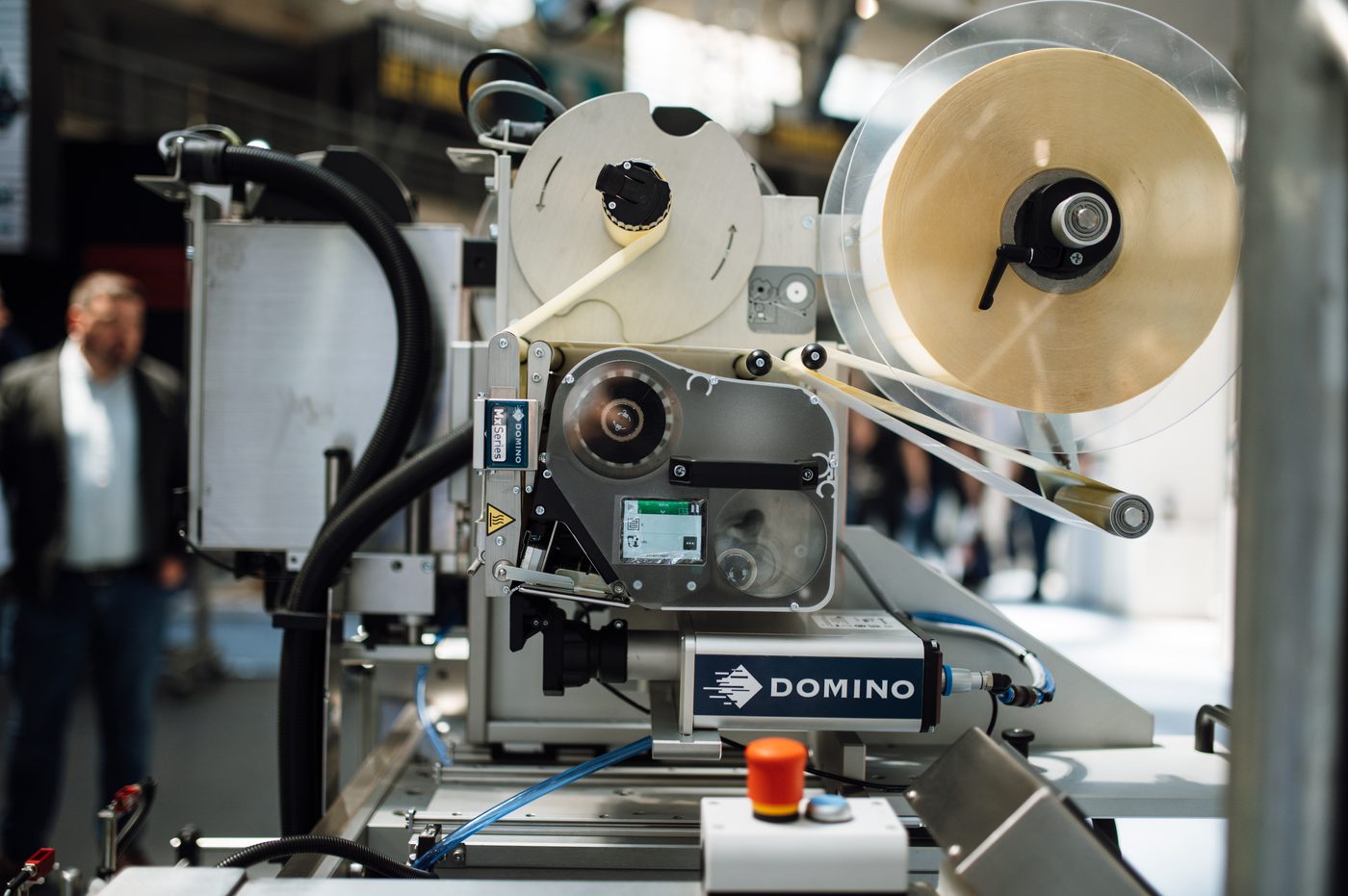 A label applicator running on a packaging line, with the label web and tape reel feeding through.