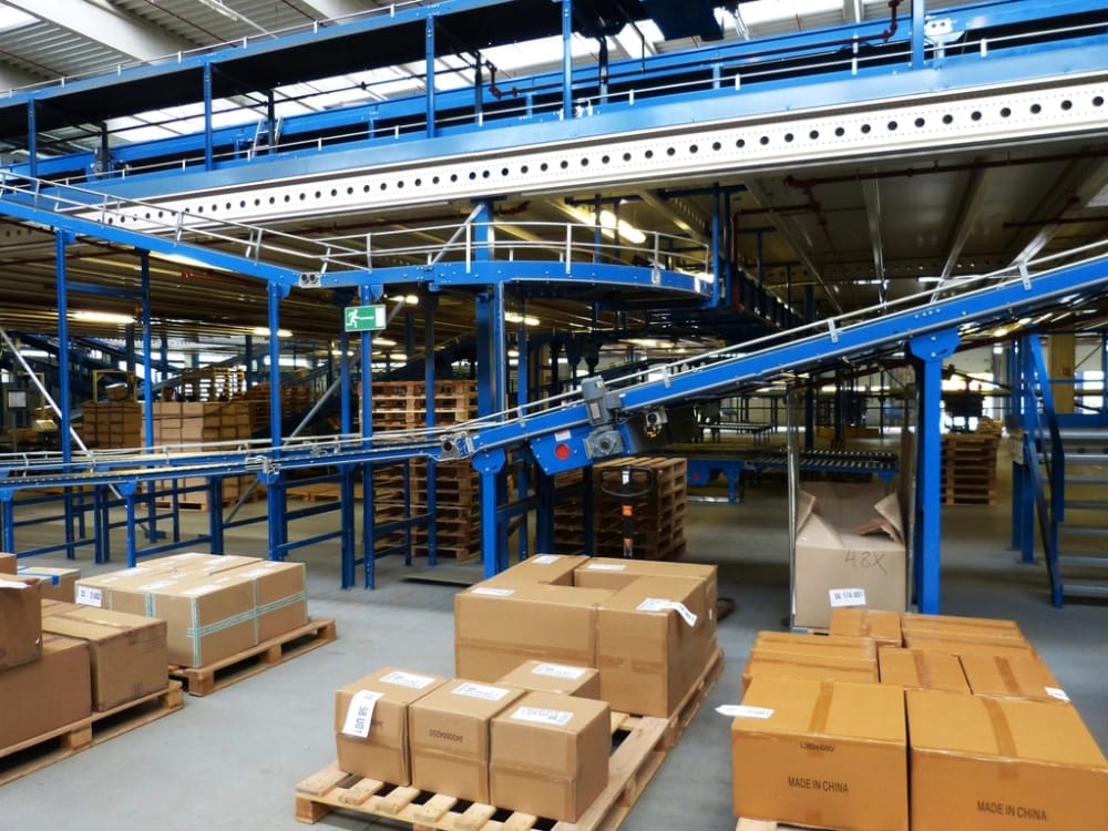 Cartons staged on pallets beside a conveyor in a receiving area, with one box opened for triage.