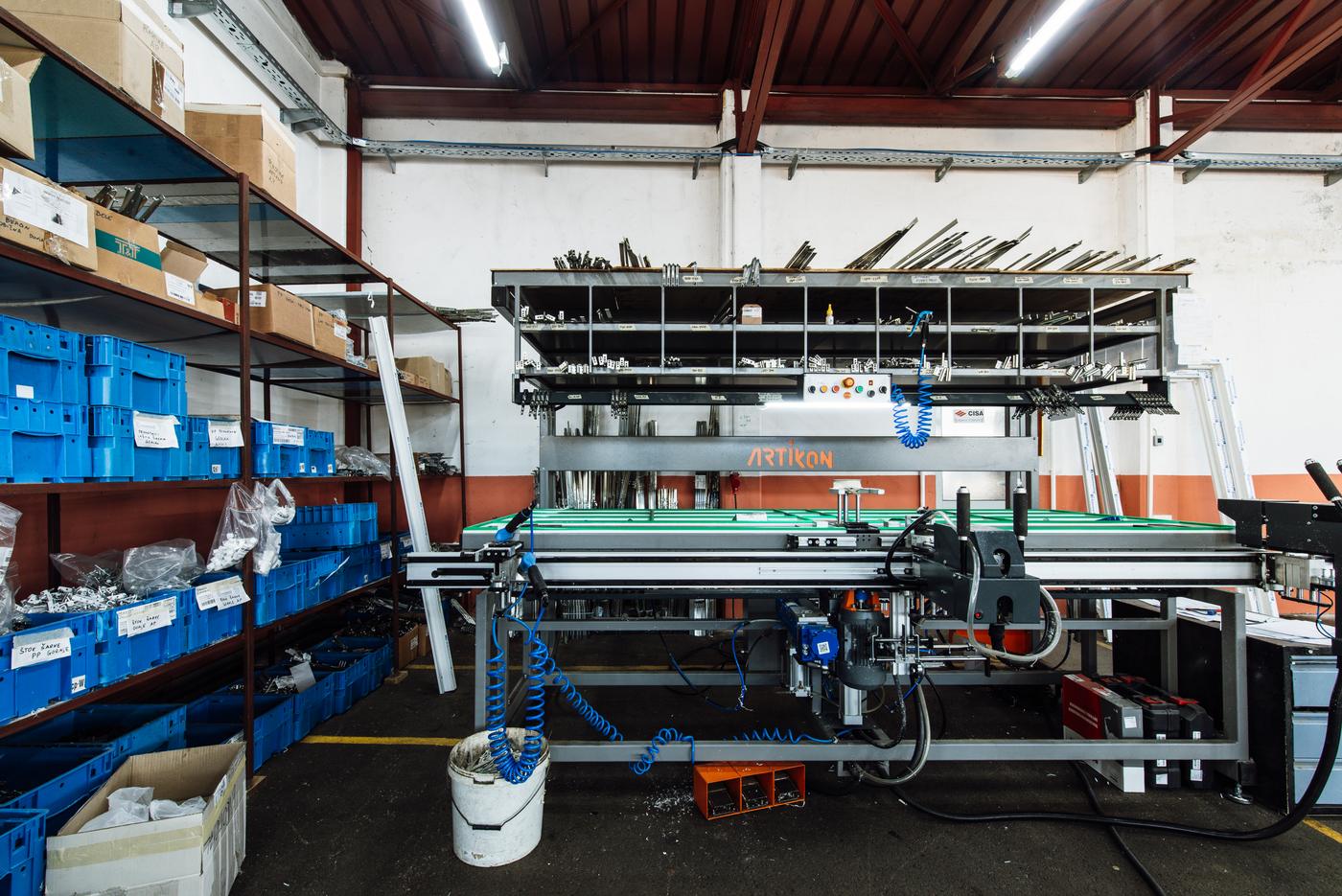 A well-organised factory workshop with labelled component bins on shelving beside a machine bay.